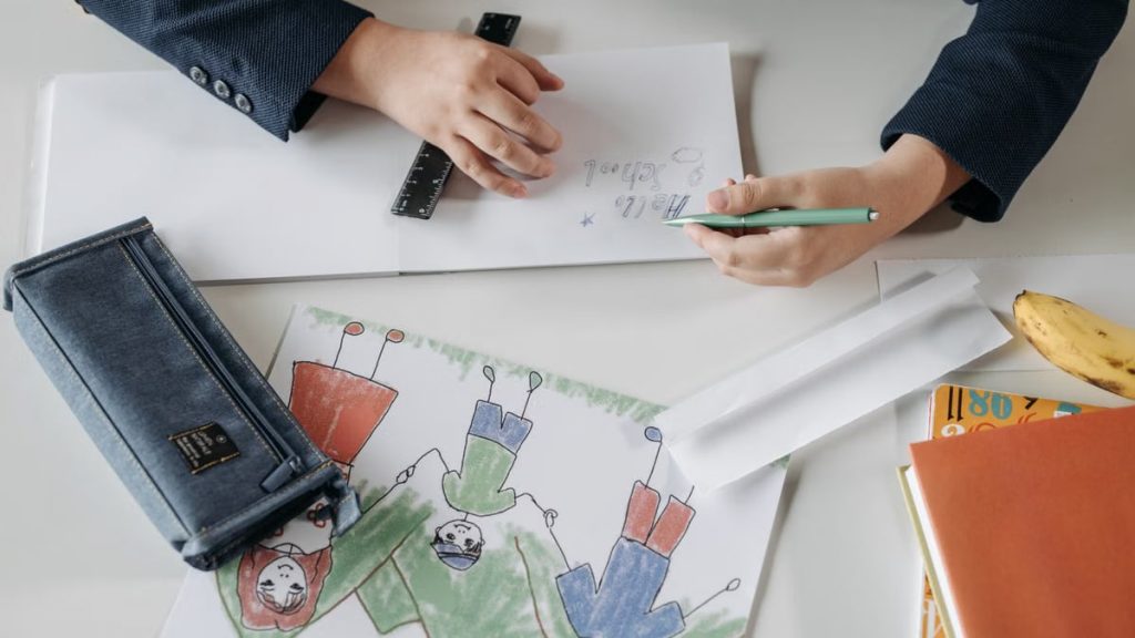 A child drawing with a pencil on a notebook, showing creativity and fine motor skills.
