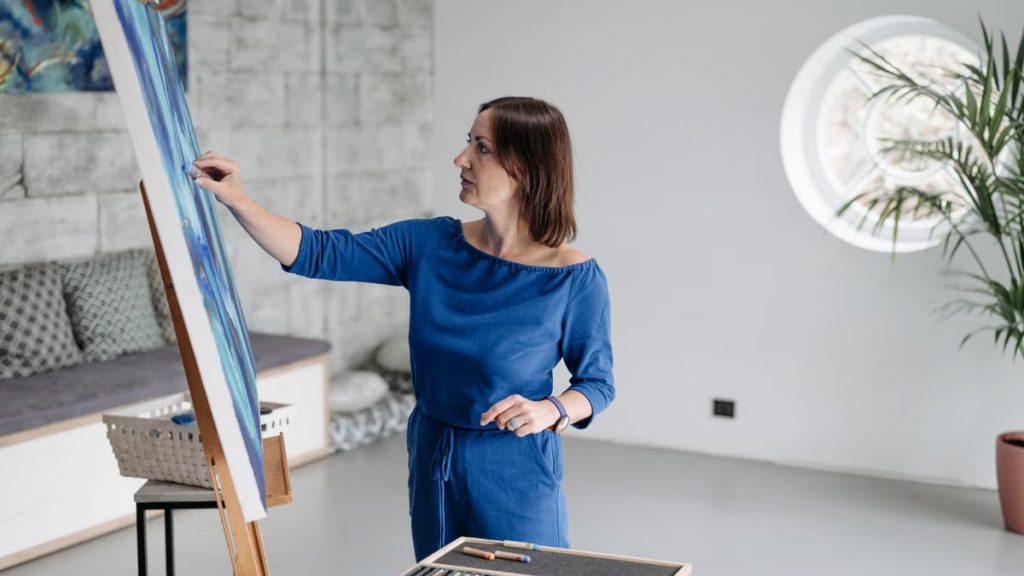 An adult woman paints on a canvas inside a modern, bright studio room.